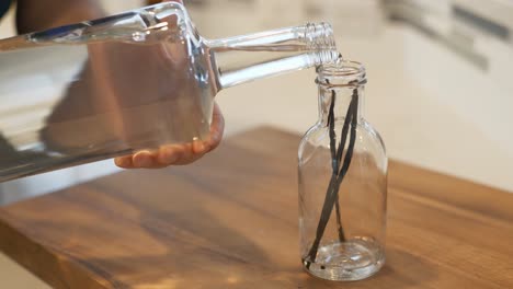 Hand-pouring-vodka-into-a-glass-jar-with-three-vanilla-beans-it-it-to-make-homemade-vanilla
