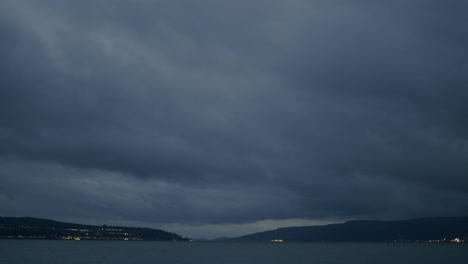 Timelapse-of-heavy-blue-clouds-passing-and-boats-in-the-distance-speeding-past-with-their-lights-on