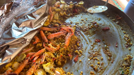 Scooping-a-traditional-Spanish-seafood-Paella-dish-with-shrimps,-St-Jacques-scallops-and-Cigala-Norway-lobsters-Nephrops-norvegicus,-cooked-rice-with-seafood,-Marbella-Spain,-4K-shot