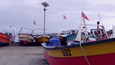 Wooden-fishing-boats-with-flags-of-Chile-in-storage-lot-on-ocean-coast