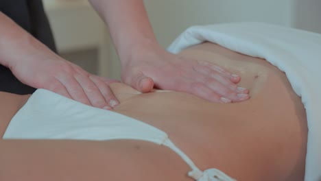 Close-up-of-two-hands-of-a-masseuse-kneading-the-stomach-of-a-client,-she-is-in-a-swimsuit
