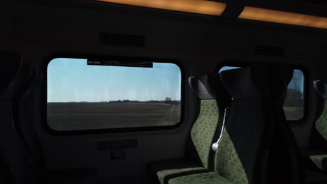 Travellers-perspective-from-the-interior-of-a-moving-train,-looking-out-to-the-countryside-passing-by