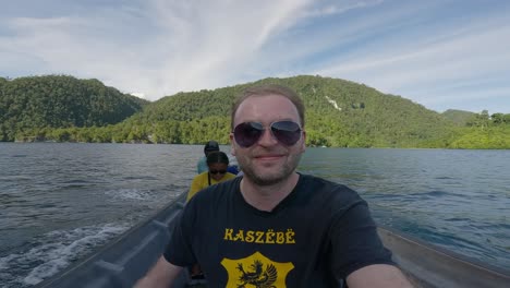 Man-in-Kaszebe-shirt-sits-in-a-boat-navigating-along-famous-blue-river-Kali-Biru