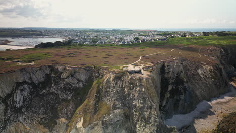 Rückwärtsbogen-Luftaufnahme-Zeigt-Verlassenen-Bunker-Auf-Einer-Klippe-Mit-Meer-Und-Stadt-Im-Hintergrund