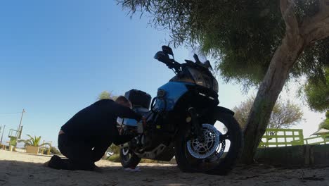 Motorcyclist-adds-motor-oil-to-motorcycle-in-shade-of-tree-outside