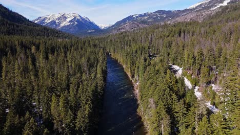 Toma-Panorámica-Hacia-Atrás-Del-Río-Y-El-Bosque-Siempre-Verde-Con-Montañas-Cubiertas-De-Nieve-Al-Fondo-En-Cle-Elum-En-Un-Día-Claro-En-El-Estado-De-Washington