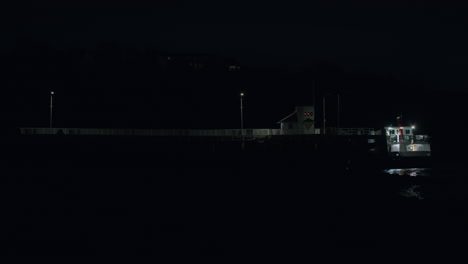 Ferry-boat-waiting-at-long-pier-at-night,-distant-static-shot