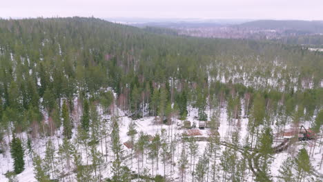 Truck-hauls-felled-timber-logs-over-snowy-forest-road-in-Sweden,-aerial-pan