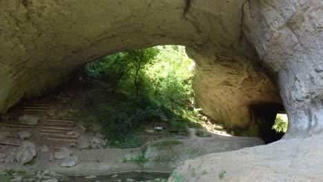 Fly-through-drone-shot-of-the-opening-of-Phodna-Cave,-right-under-the-natural-arch-called-Gods-Bridge,-located-in-a-geological-park-in-Karlukovo,-Bulgaria