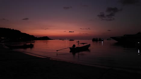Multiple-boats-moored-in-sheltered-beach-on-tropical-island,-shot-during-beautiful-pink-and-orange-sunset