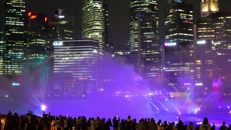Magical-evening-with-vibrant-visual-effect-SPECTRA-light-and-water-show-with-misty-spray-and-light-projects-against-downtown-cityscape,-time-lapse-shot-capturing-crowds-at-Marina-Bay-Sands-event-plaza