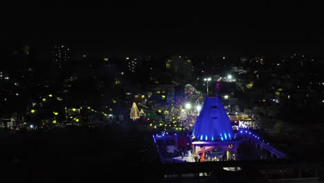 La-Cámara-Del-Teléfono-Con-Vista-Aérea-De-Drones-Vuela-Detrás-Del-Templo-Y-Muchas-Casas-Son-Visibles-Con-Luces-Sony-Y-Muchos-Edificios-Residenciales-También-Están-Allí.