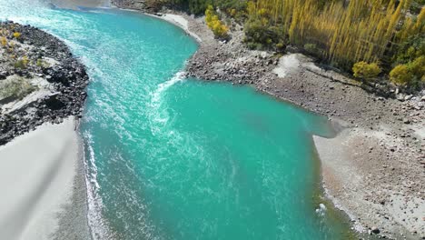 Aerial-View-Of-Flowing-Turquoise-Indus-River-With-Tilt-Up-Reveal-Of-Autumnal-Trees-In-Skardu-Valley