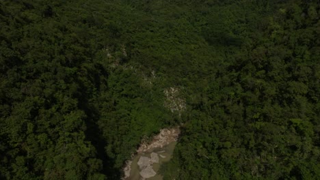 Flying-over-river-flowing-between-Muchas-Aguas-mountains,-San-Cristobal-in-Dominican-Republic