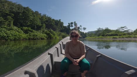 Frau-Sitzt-Auf-Bugboot,-Das-Entlang-Des-Berühmten-Blauen-Flusses-Kali-Biru-In-Indonesien-Navigiert,-Umgeben-Von-üppiger-Vegetation