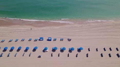 Atemberaubende-Aussicht-Auf-Liegestühle-Und-Sonnenschirme-Fliegen-über-Den-Sand-Und-Das-Blaue-Strandwasser-Blauer-Himmel-Palmen-Ft