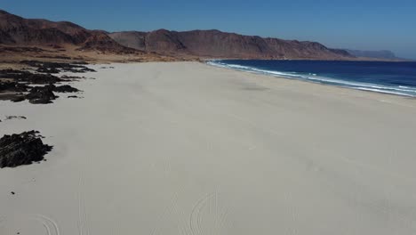 Aerial-tilts-from-rugged-rocks-to-expansive-Atacama-sandy-ocean-beach