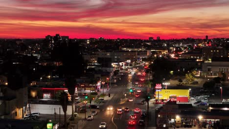 Aerial-reverse-flight-pointing-west-with-a-crimson-red-sky-over-the-Talmadge-section-of-El-Cajon-Boulevard-in-San-Diego-with-traffic-flowing-in-both-directions-at-dusk-just-past-sunset
