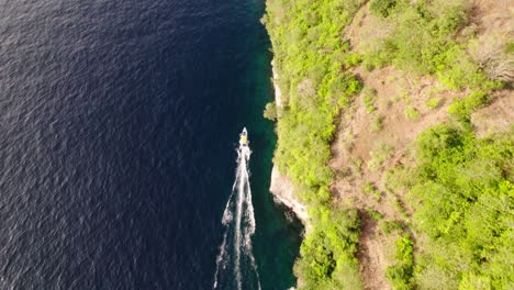 Boat-Cruising-On-Turquoise-Sea-By-Lush-Green-Island-In-Nusa-Penida,-Bali,-Indonesia