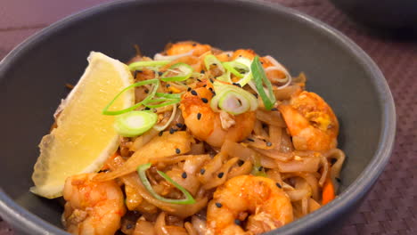 Traditional-Pad-Thai-wok-noodles-with-shrimps,-spring-onion-and-a-lemon-slice,-Thai-restaurant,-delicious-Asian-food,-4K-shot