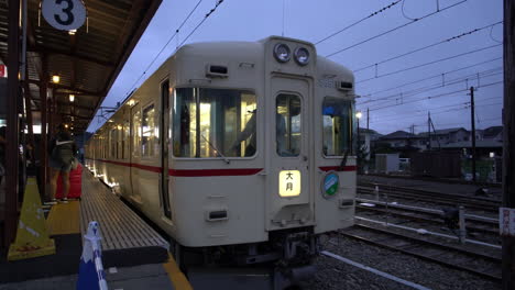 A-uniformed-worker-stands-beside-a-stopped-train,-his-arm-raised-making-signals-at-Kawaguchiko-Station