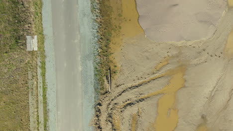 Top-down-view-of-a-road-adjacent-to-a-sandy-embankment-with-visible-layers-of-aggregate-materials,-showcasing-the-elements-of-road-construction