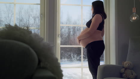 Pregnant-woman-in-bra-waiting-for-baby,-looking-at-winter-landscape