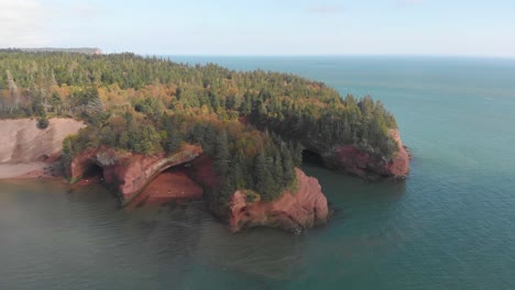 Slow-aerial-decent-showcasing-a-stunning-cliff-with-trees-on-it-in-St,-Martins,-New-Brunswick