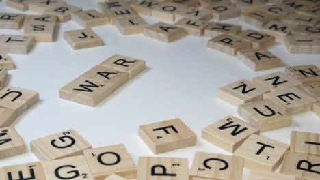Finger-Bilden-Wortkrieg-Auf-Weißer-Tischplatte-Mit-Scrabble-Buchstabensteinen