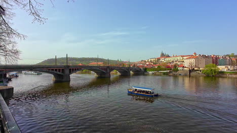 Tourist-boat-sails-under-bridge-on-Vltava-river-in-Prague,-static-view