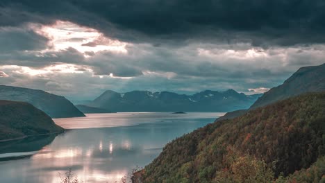 Rays-of-the-setting-sun-shine-through-stormy-clouds-over-a-calm-fjord-in-a-time-lapse-video