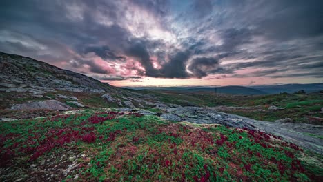 Whirling-dark-stormy-clouds-backlit-by-the-red-setting-sun-hover-above-the-colorful-autumn-tundra-landscape