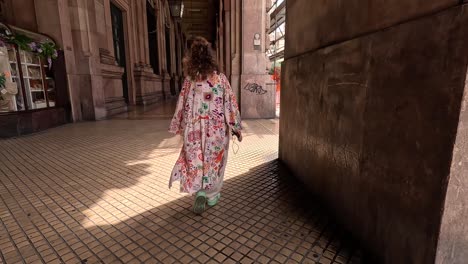 Woman-wearing-flowing-patterned-clothing-walking-along-covered-archway
