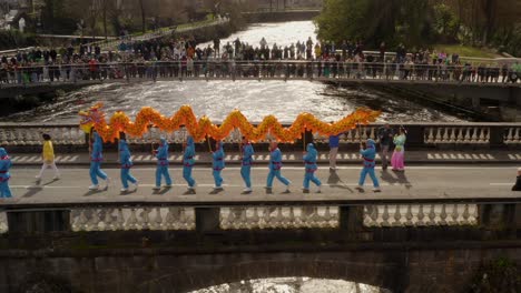 Ein-Leuchtend-Goldgelber,-Orangefarbener-Drache-Läuft-Während-Einer-Lebhaften-Kulturparade-Die-Salmon-Weir-Bridge-Entlang