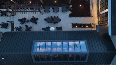 Top-down-view-of-a-cafe-terrace-with-black-tables-and-chairs,-string-lights,-and-an-awning