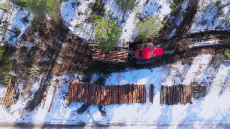 Forwarder-with-grapple-loader-transports-felled-logs-alongs-snowy-track,-aerial