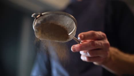 Close-up-slow-motion-clip-of-a-chef's-hand-tapping-the-handle-of-a-sieve-to-sprinkle-cocoa-powder