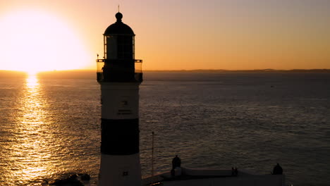 Aerial-view-of-Farol-da-Barra-illuminated-by-the-sun-and-the-sea,-at-sunset,-Salvador,-Bahia,-Brazil