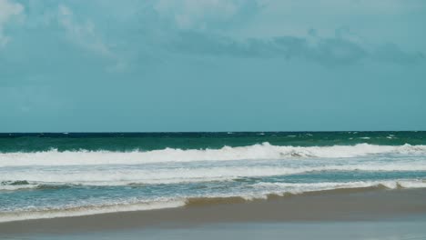 La-Pintoresca-Vista-De-Una-Playa-Tropical,-Con-Olas-Suaves-Y-Un-Telón-De-Fondo-De-Cielos-Azules-Intensos