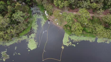 Drone-descending-over-a-lake-with-a-safe-swimming-spot-with-safety-net-and-kayaks-visible-on-the-water