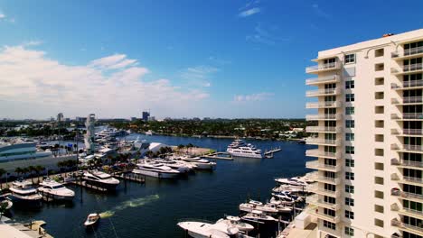 Nice-aerial-shot-of-yachts-and-boats-in-the-water-flying-past-a-building-blue-sky-white-clouds-ft