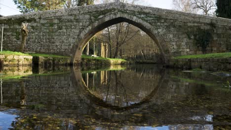 Puente-Sereno-Reflejo-En-Aguas-Poco-Profundas-Del-Río-Debajo-Del-Puente-Romano-Medieval-En-El-Campo-Español