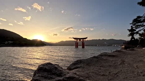 Sunset-timelapse-showcasing-Itsukushima-Shrine's-torii-gate-in-Japan,-with-sunlight-reflecting-off-the-water's-surface