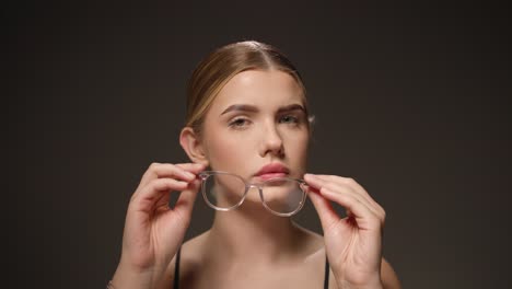 Cute-woman-breathes-on-transparent-glasses-to-clean-them,-portrait-studio-shot