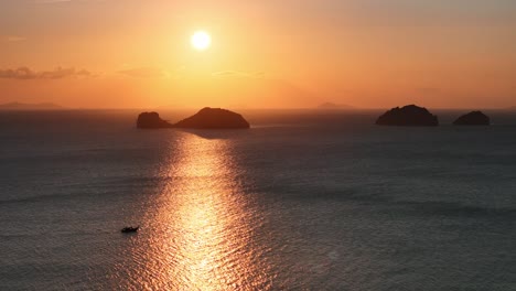 Sun-going-down-at-the-sea,-shining-a-boat-among-the-islands-in-a-distance