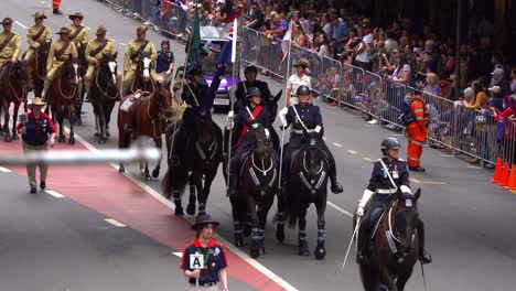 Queensland-Police-Service-Mounted-Unit-riding-down-the-street-during-the-Anzac-Day-parade,-cheering-by-the-crowds-along-the-street-with-cheering-crowds-along-the-street