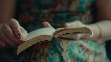 front-view-of-senior-woman-turning-page-of-a-book-while-sitting-and-reading-in-her-living-room-house