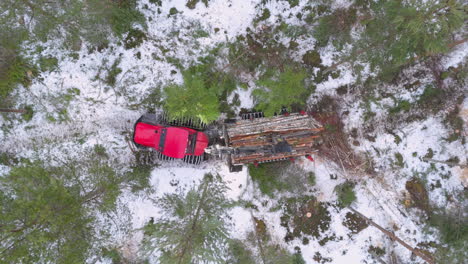 Forwarder-with-grapple-loader-transports-felled-logs-in-snowy-forest,-top-drone
