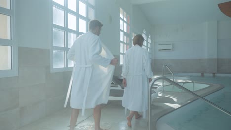 Slow-motion-shot-of-a-couple-taking-off-robes-ready-to-head-into-the-pool