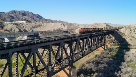 Freight-Train-Carrying-Cargo-Crossing-Over-Steel-Frame-Bridge,Boarder-Between-California-and-Arizona-,-Colorado-River-,-I-40-freeway-East,-Establishing-Tracking-Cinematic-Aerial